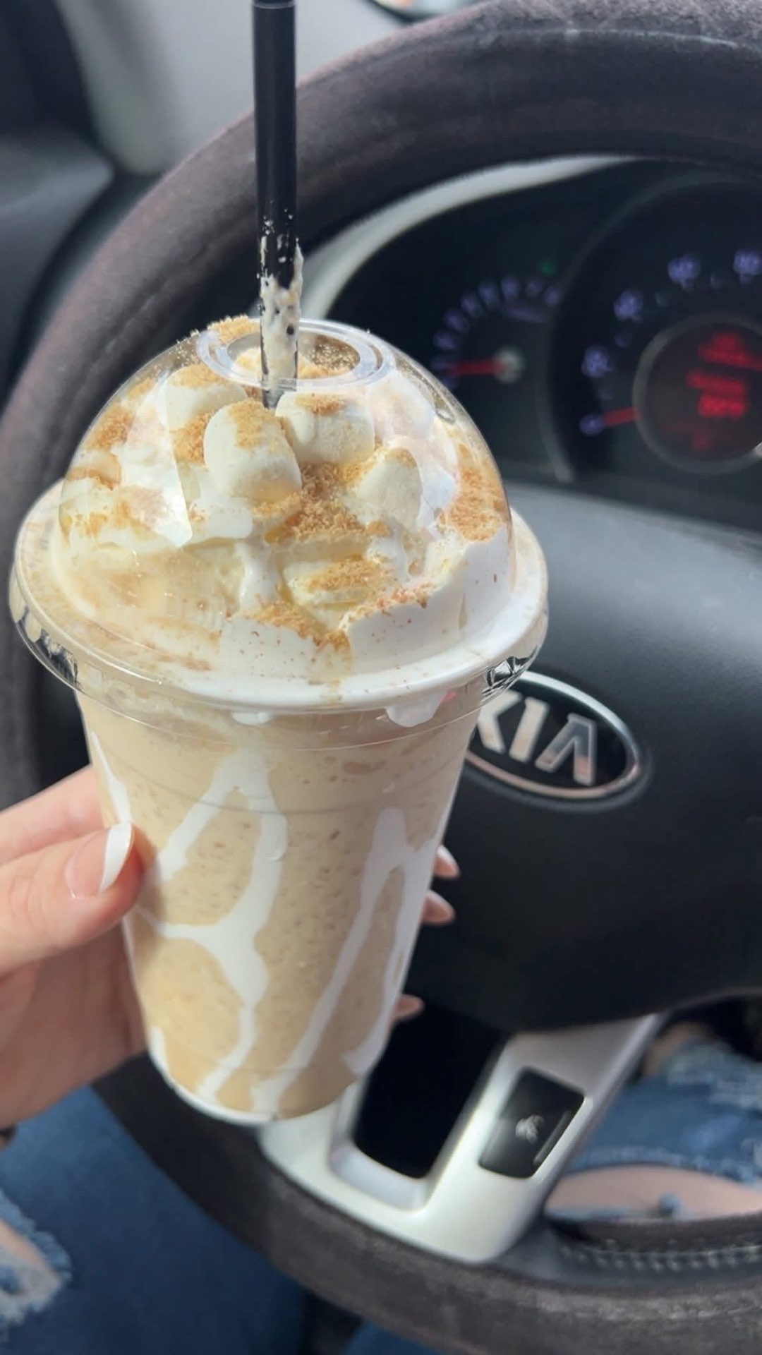 A marshmallow-topped iced coffee resting on a Kia steering wheel.